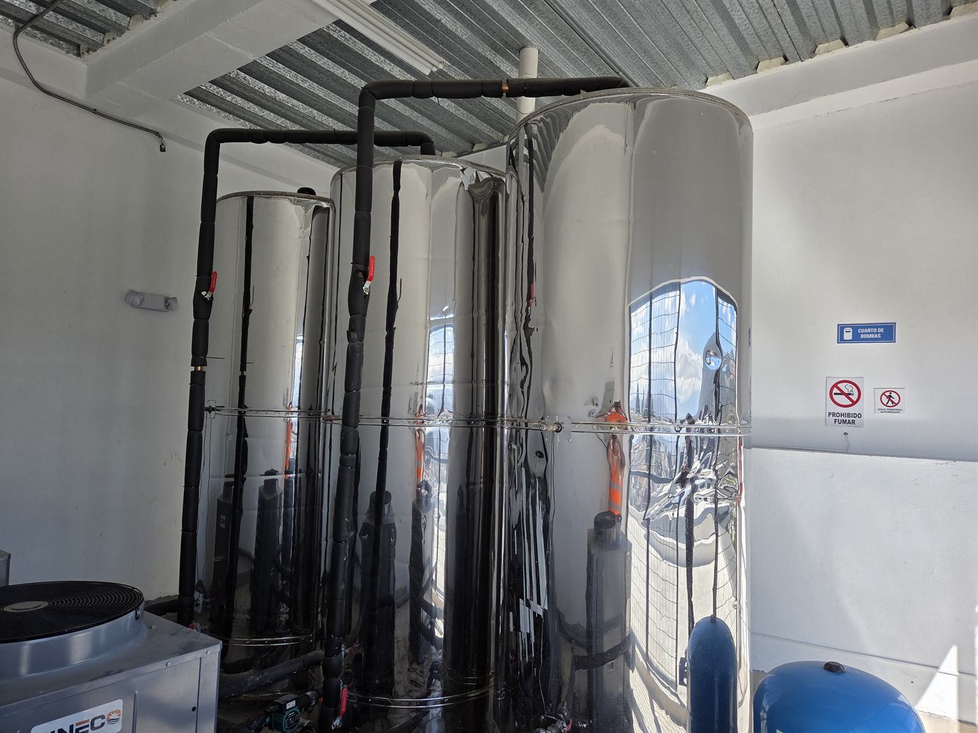 Cuarto de bombas de un edificio con tres acumuladores de acero inoxidable, tubería aislada y una unidad de bomba de calor
