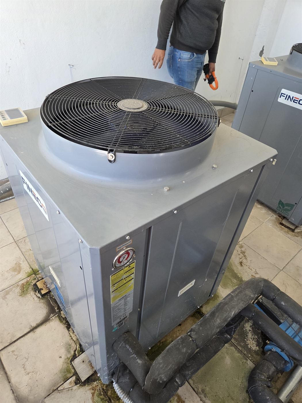Unidad exterior de bomba de calor FINEC con tubería hidráulica aislada y técnico junto al equipo