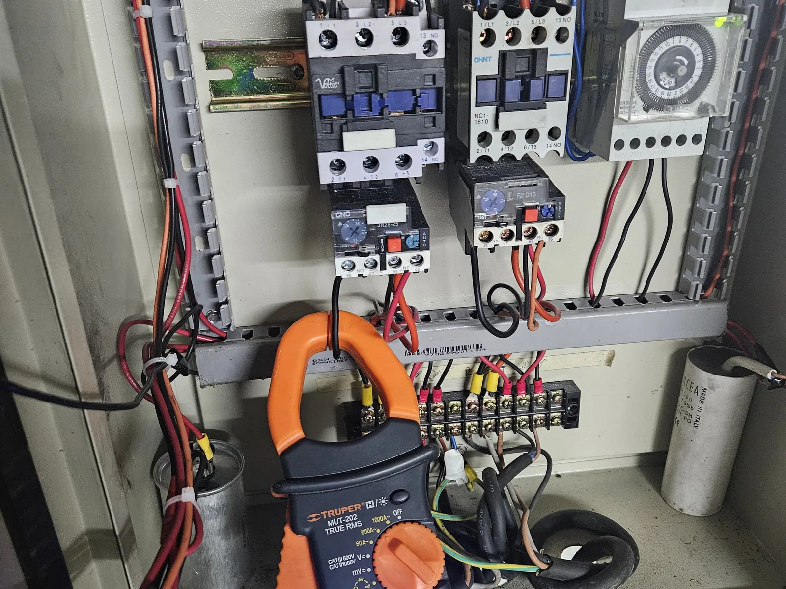 Pinza amperimétrica colocada junto a contactores y borneras de un tablero eléctrico