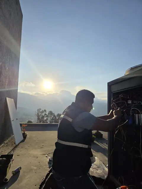 Técnico electromecánico revisando conexiones de equipo de climatización en terraza al atardecer en Quito